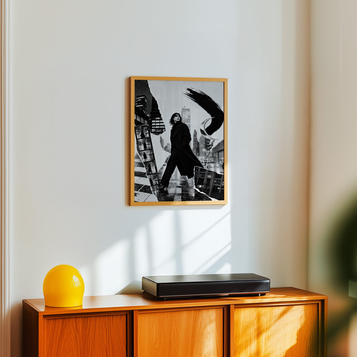 Woman in black coat torn paper collage print in an oak frame above a teak sideboard with a yellow glass lamp