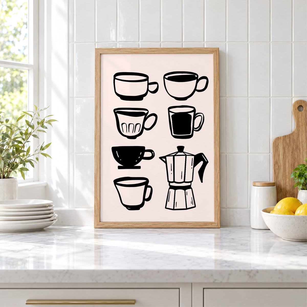 Black coffee cups and moka pot print in an oak frame leaning on a marble counter by white tiles and lemons
