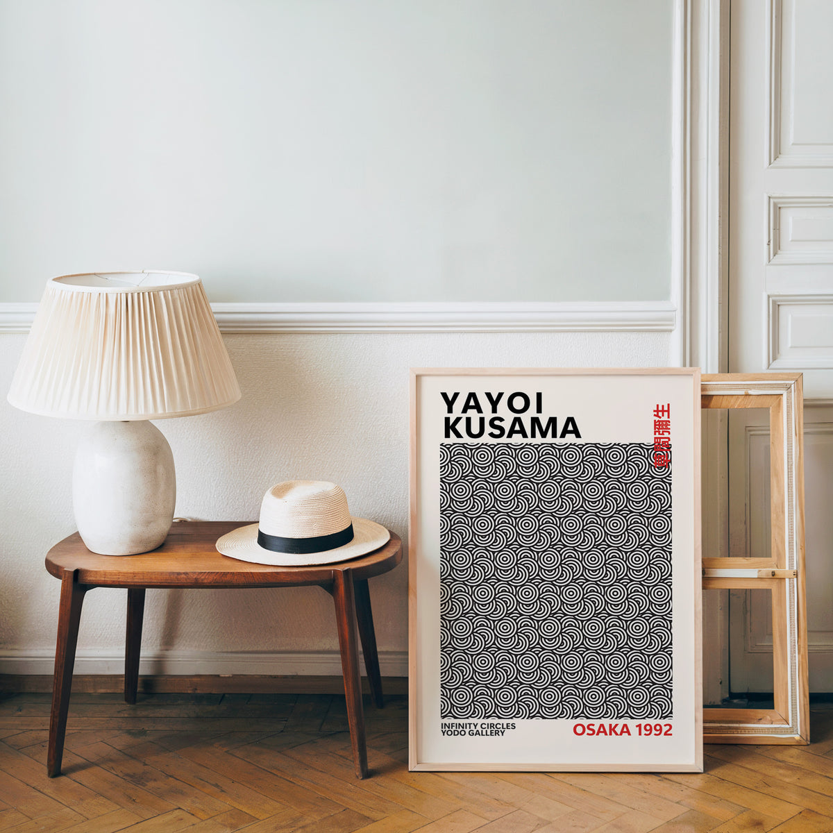 Yayoi Kusama inspired black concentric circles print leaning beside a wooden bench with a lamp and straw hat