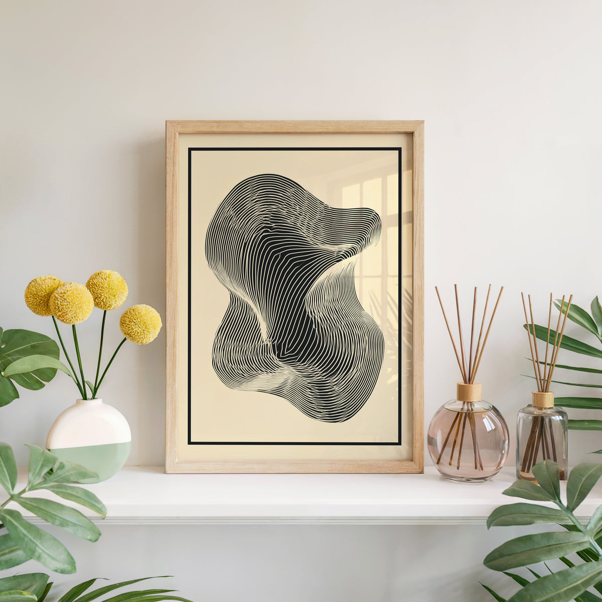 Black contour line blob minimalist op art print in a light oak frame leaning on a white mantel with yellow flowers