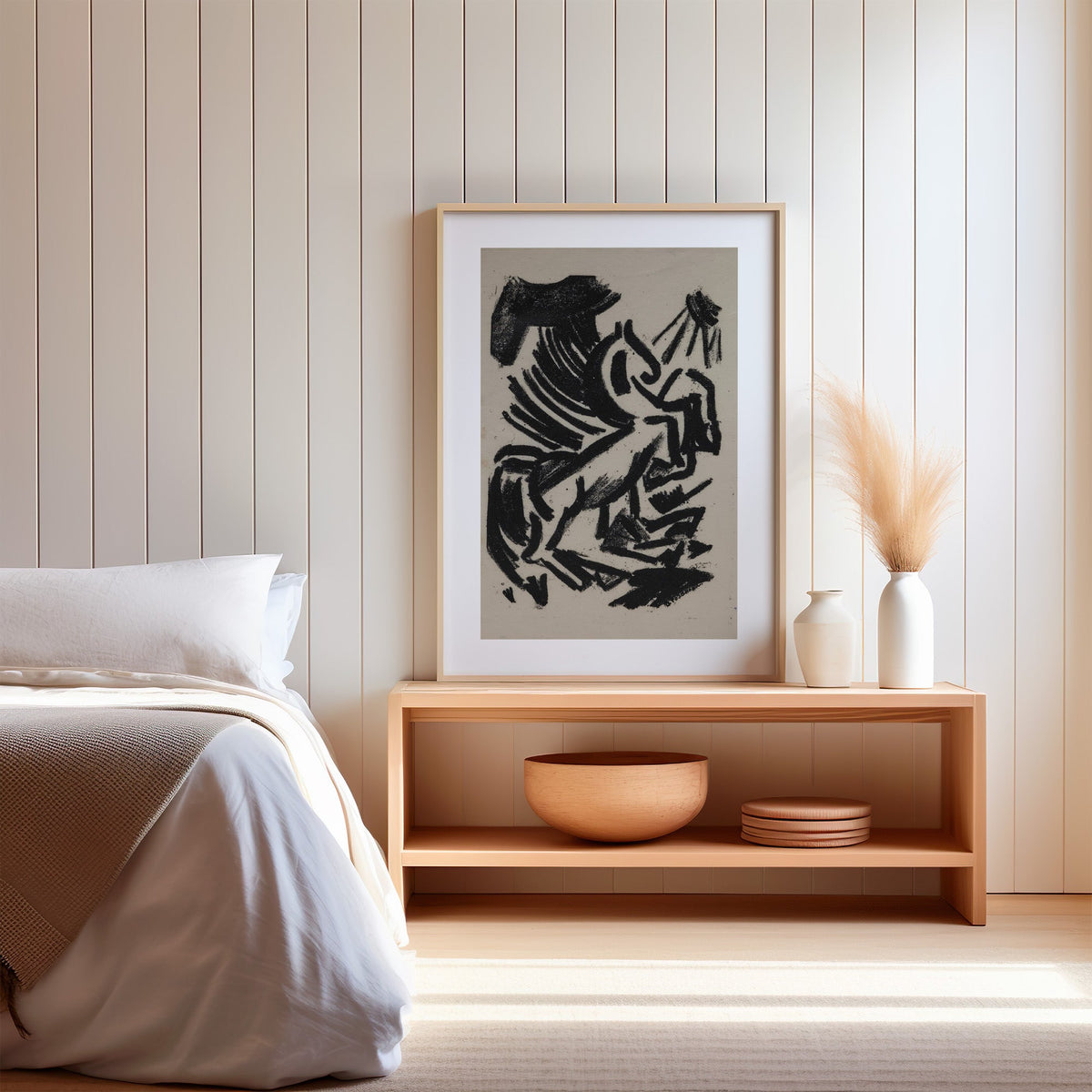 Black crayon rearing animal and sun print in a light oak frame on a wood bench by a bed with pampas grass