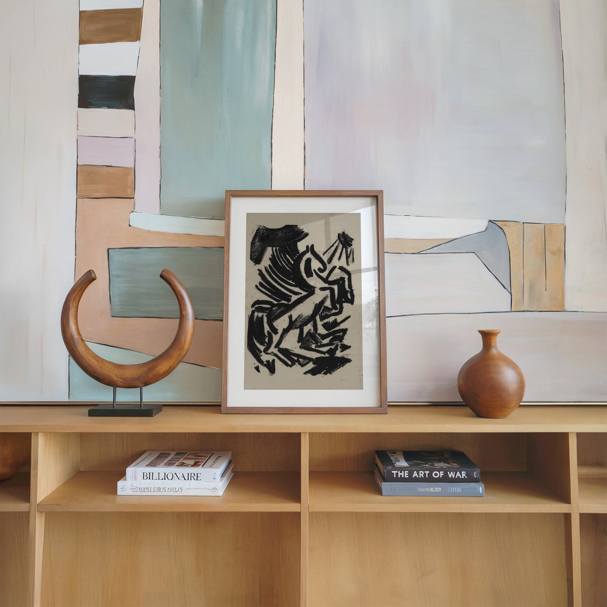 Black crayon rearing animal and sun print in a walnut frame on an oak shelf beside a wooden crescent sculpture
