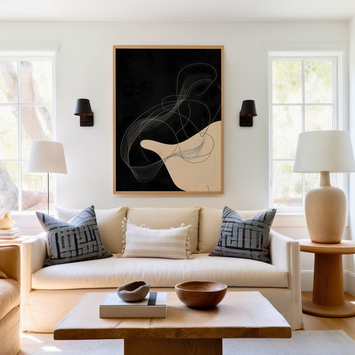 Black and cream flowing line art abstract print in a light oak frame above a cream sofa between two black wall sconces