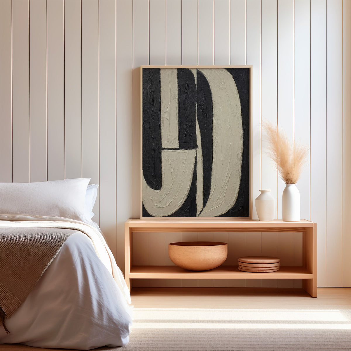 Black and cream J arch bands mid century print in a light oak frame on a wood bench by a bed with pampas grass