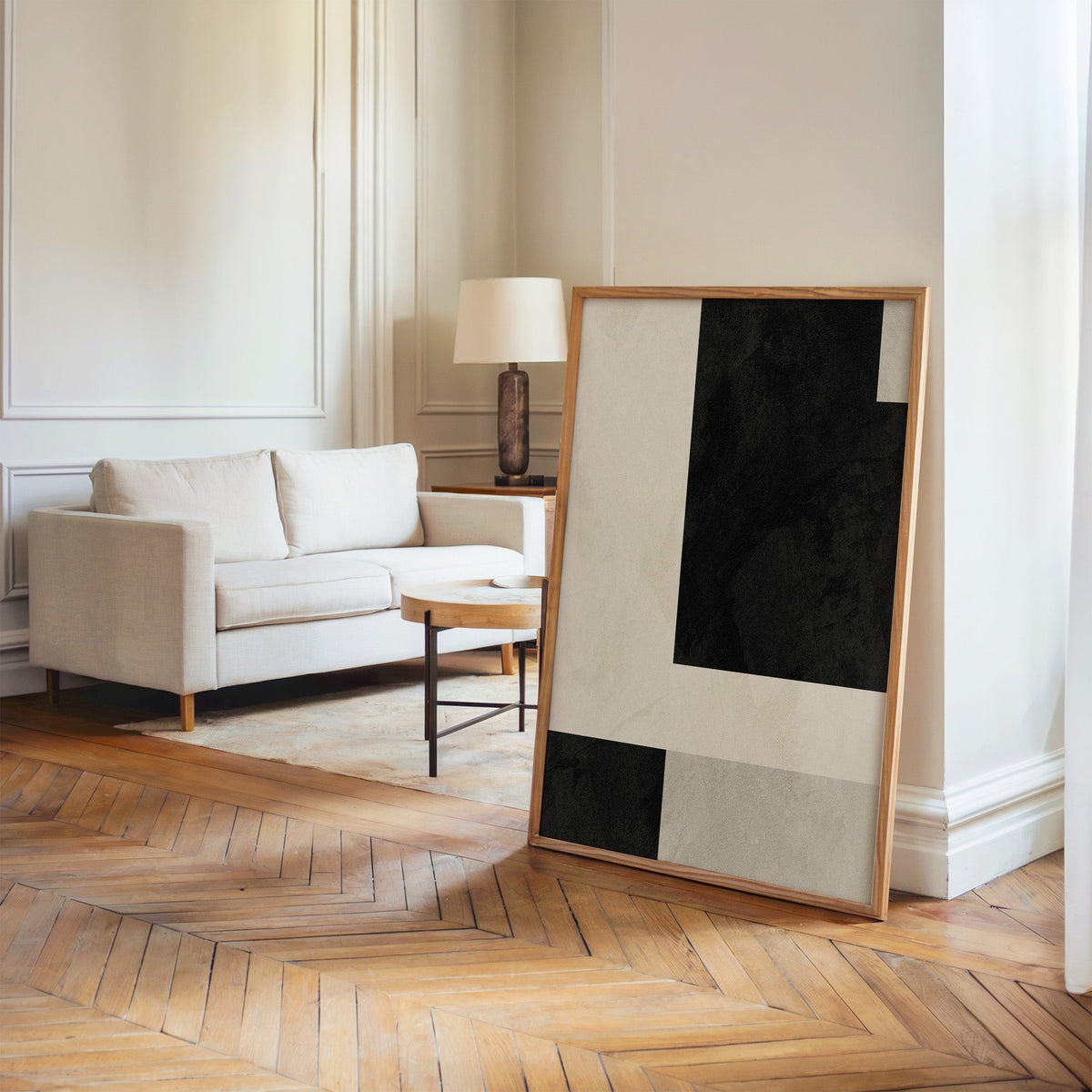 Black and cream offset plaster blocks print in an oak frame leaning on a herringbone floor by a cream linen sofa