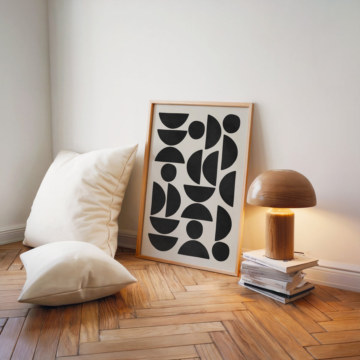 Black and cream semicircle pattern mid century print in a light wood frame on a herringbone floor by a wooden mushroom lamp