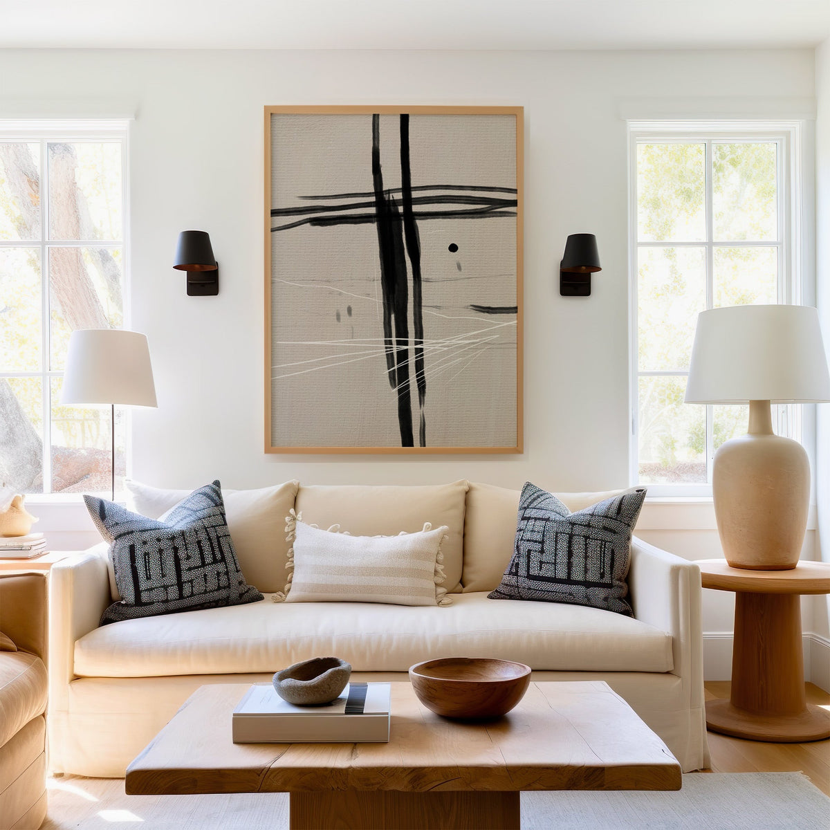 Black crossed brushstrokes and dot abstract print in a light oak frame above a cream sofa between two black wall sconces