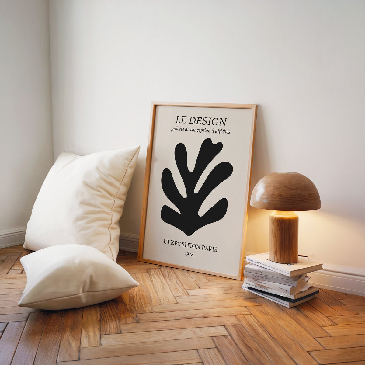 Black cutout seaweed leaf abstract botanical print in a light wood frame on a herringbone floor by a wooden mushroom lamp