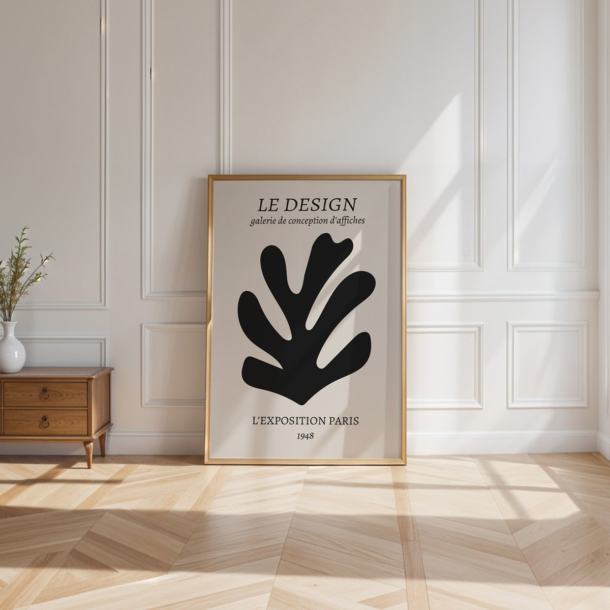 Black cutout seaweed leaf abstract botanical print shown in a gold frame leaning on a paneled white wall in sunlight
