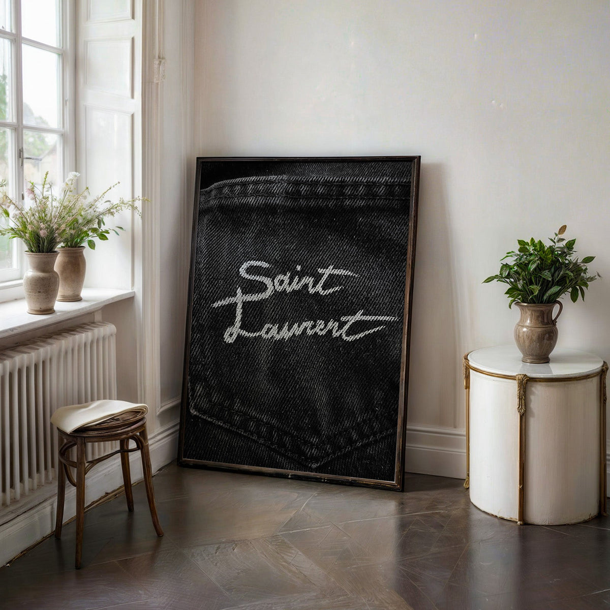 White script stitched on black denim pocket print in a black frame on a dark stone floor beside a white side table