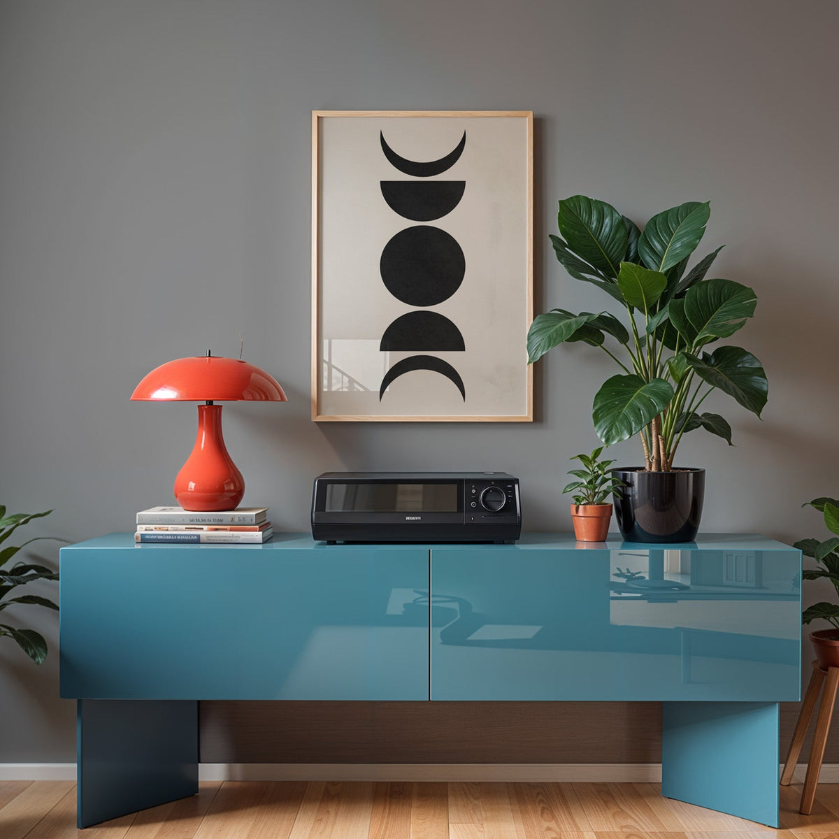 Black five moon phases minimalist print in a light oak frame above a teal sideboard with a red mushroom lamp