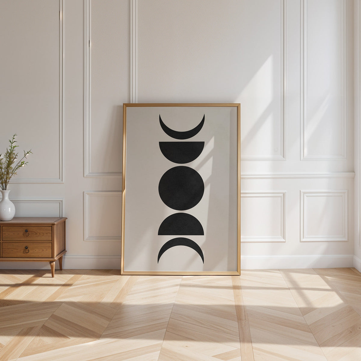 Black five moon phases minimalist print shown in a gold frame leaning on a paneled white wall in sunlight