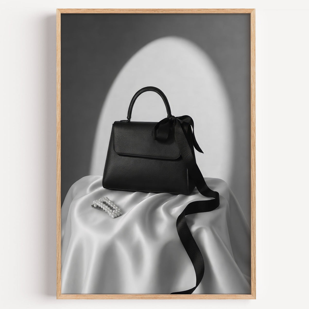 Black top-handle handbag on silk with pearl clip print in a light oak frame on a plain white wall