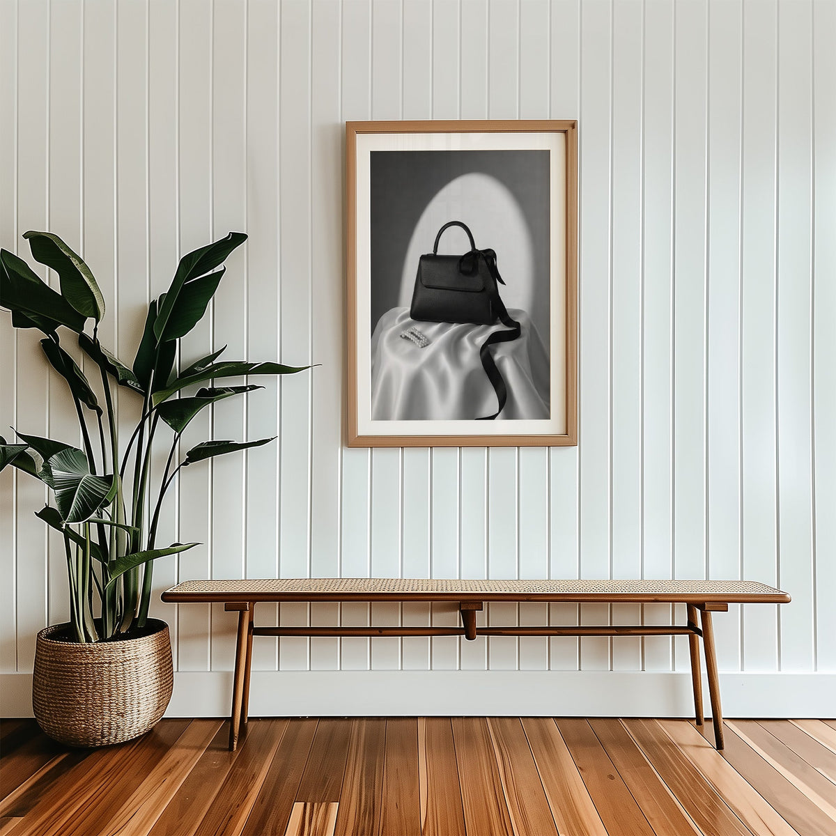 Black top-handle handbag on silk with pearl clip print in a wood frame with a white mat above a cane bench