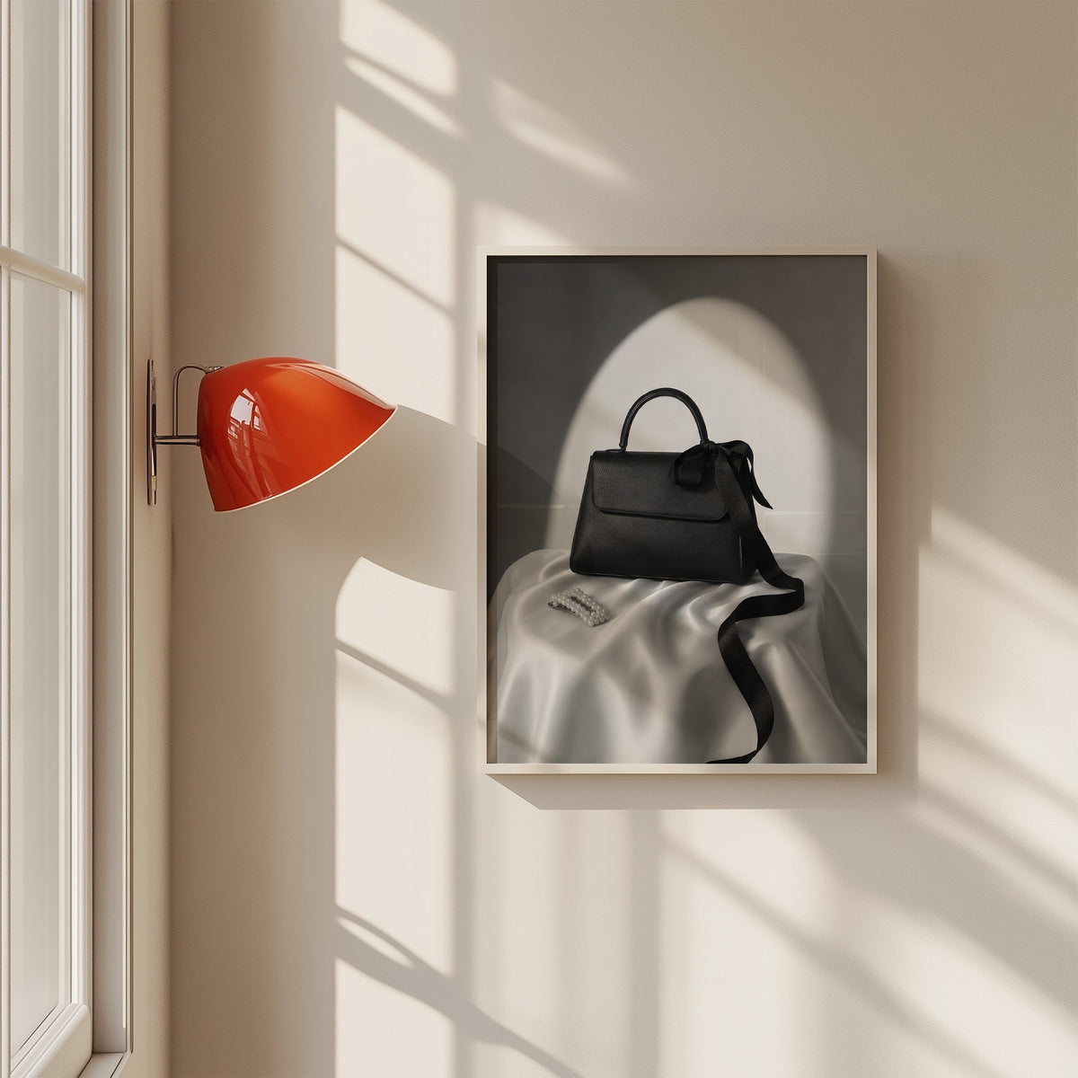 Black top-handle handbag on silk with pearl clip print in a white frame on a sunlit wall beside a red sconce