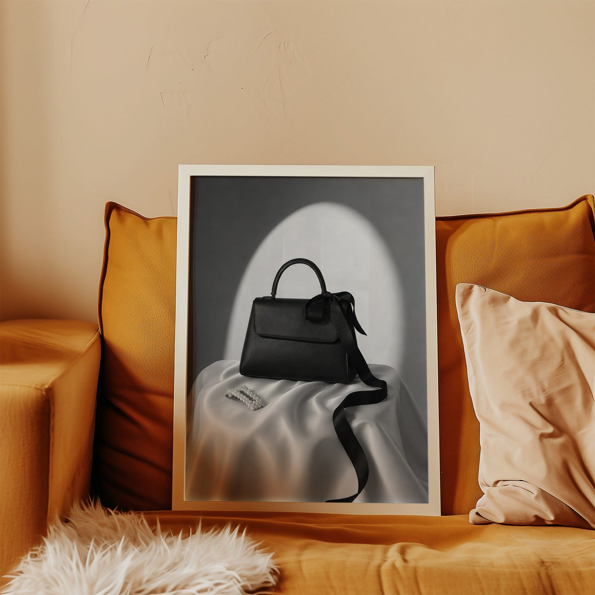 Black top-handle handbag on silk with pearl clip print in a white frame leaning on a mustard velvet sofa