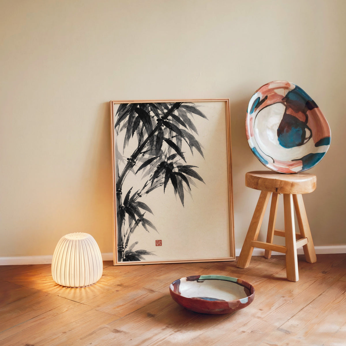 Black ink bamboo sumi-e poster in a light wood frame leaning on a wooden floor by a glowing lamp and stool