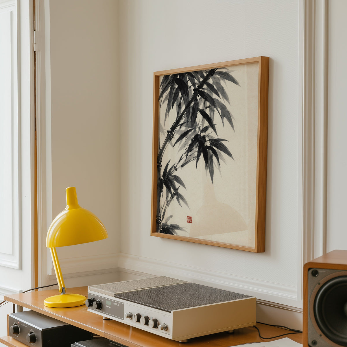 Black ink bamboo sumi-e poster in an oak frame above a vintage hi-fi shelf with a yellow desk lamp