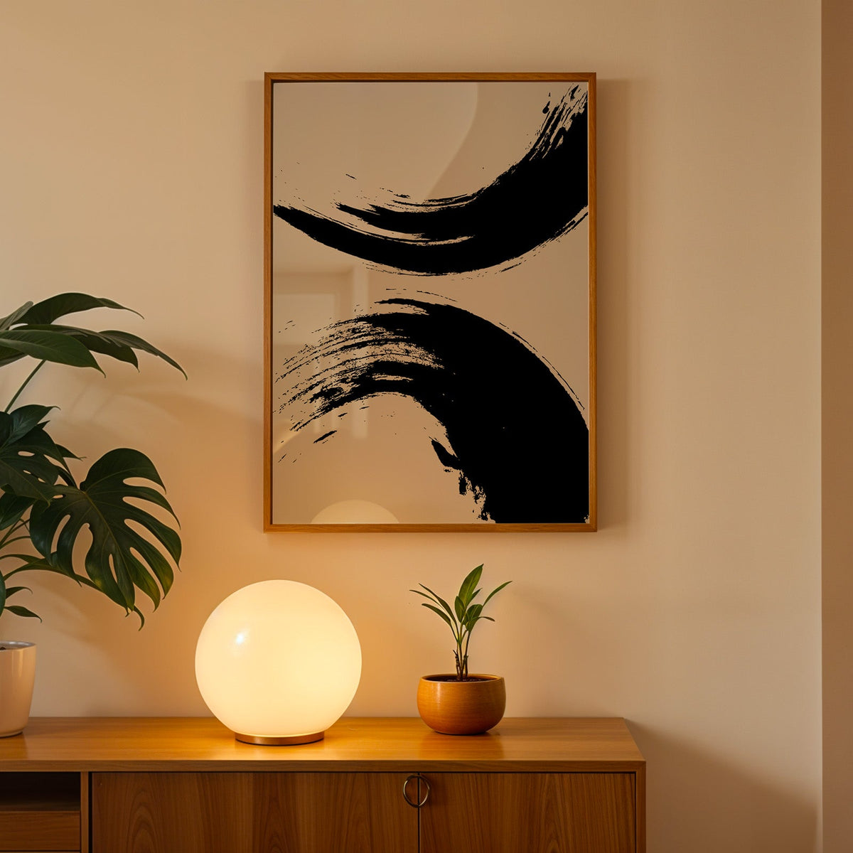 Black ink brush arcs abstract print in an oak frame above a teak cabinet with a globe lamp and monstera
