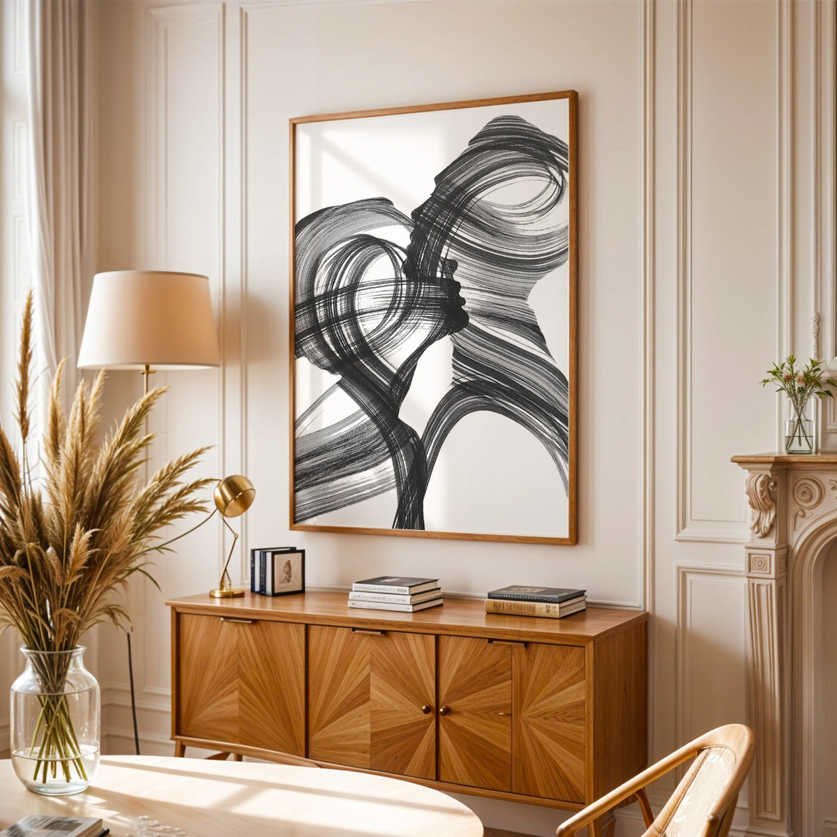 Black ink brush swirl abstract print in an oak frame above a sunburst wood sideboard with pampas grass