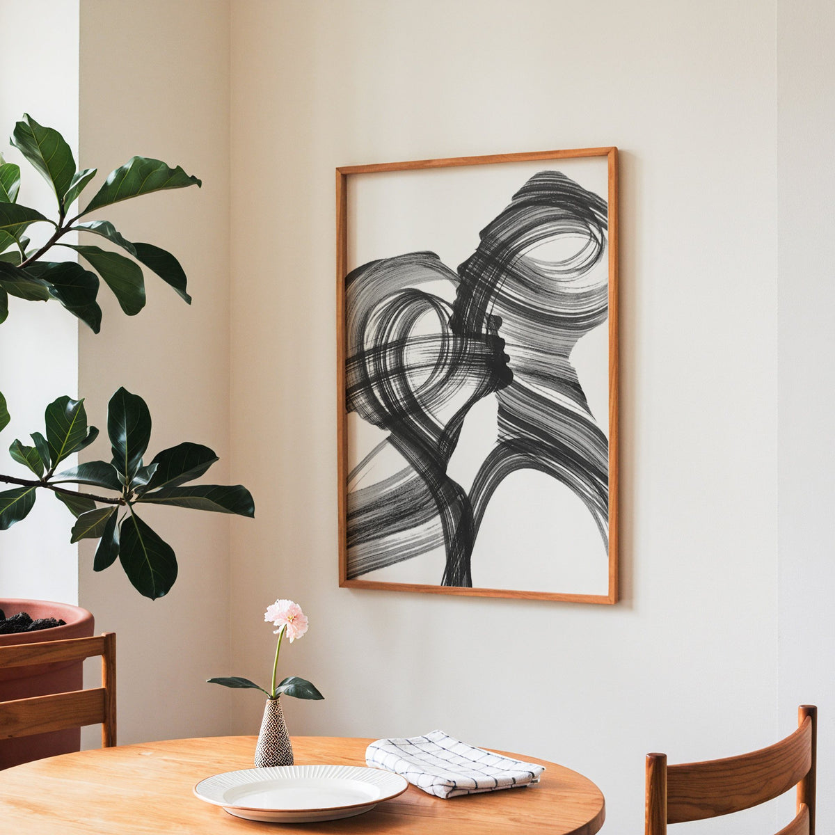 Black ink brush swirl abstract print in a teak frame above a round wooden dining table