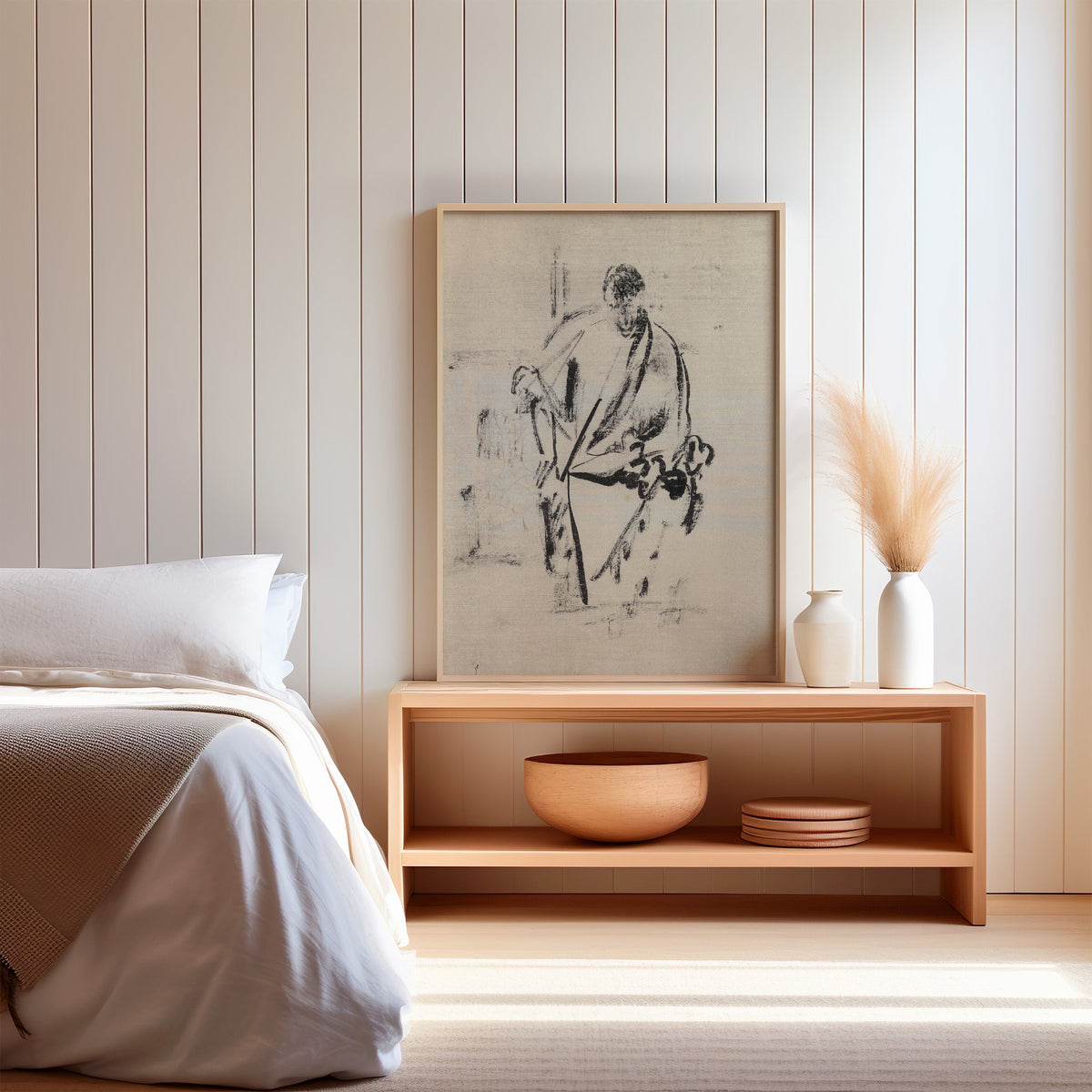 Black ink robed figure with staff sketch print in a light oak frame on a wood bench by a bed with pampas grass