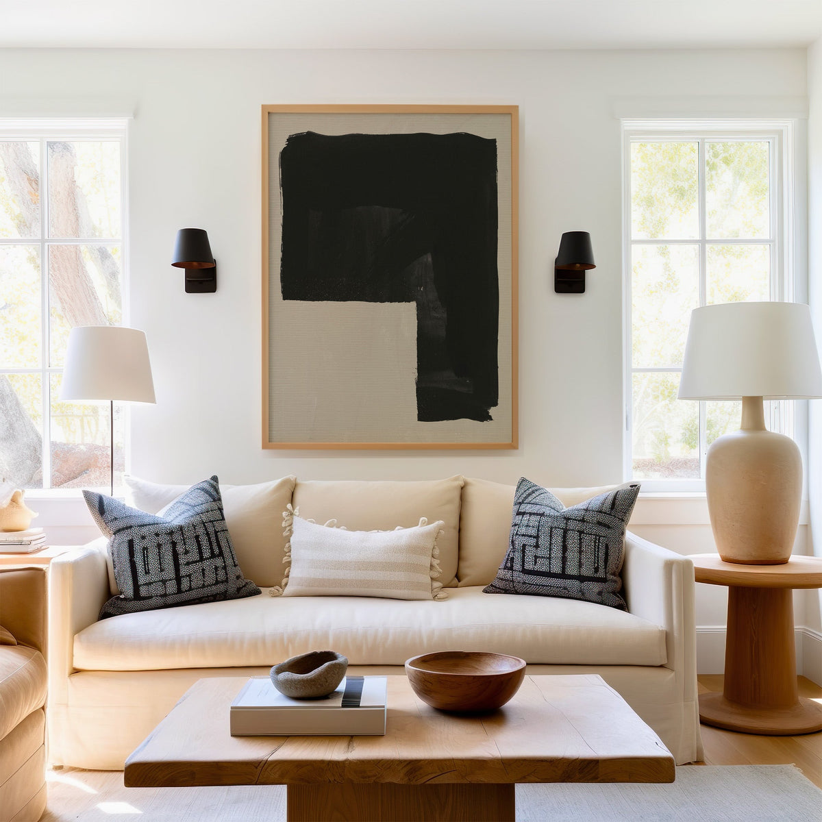 Black inverted L block on greige print in a light oak frame above a cream sofa between two black wall sconces