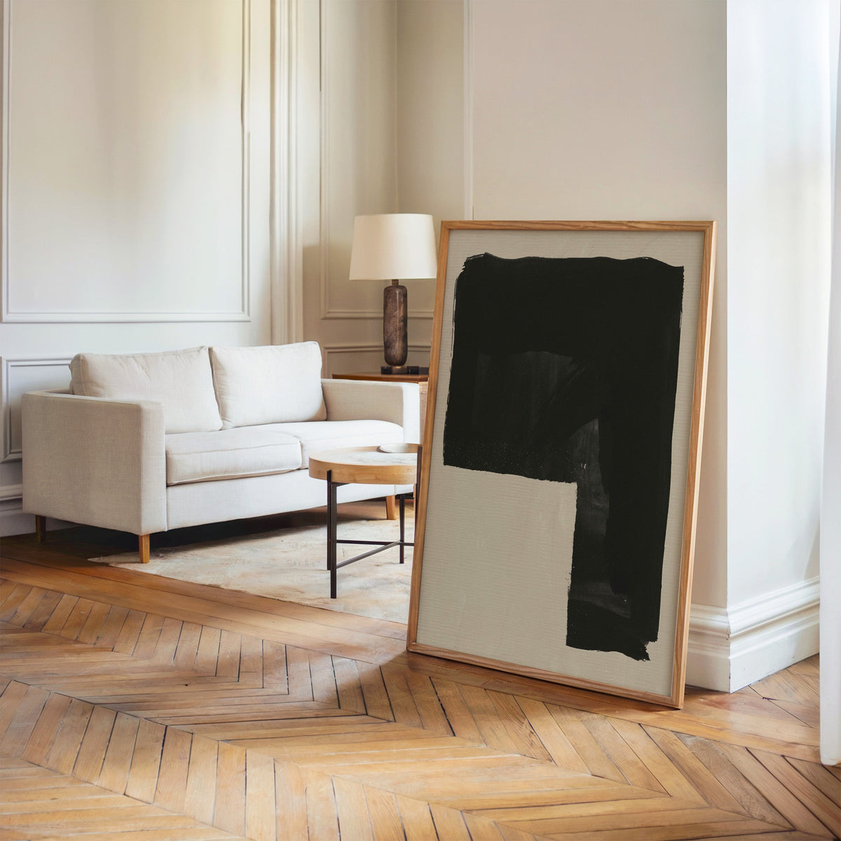 Black inverted L block on greige print in an oak frame leaning on a herringbone floor by a cream linen sofa