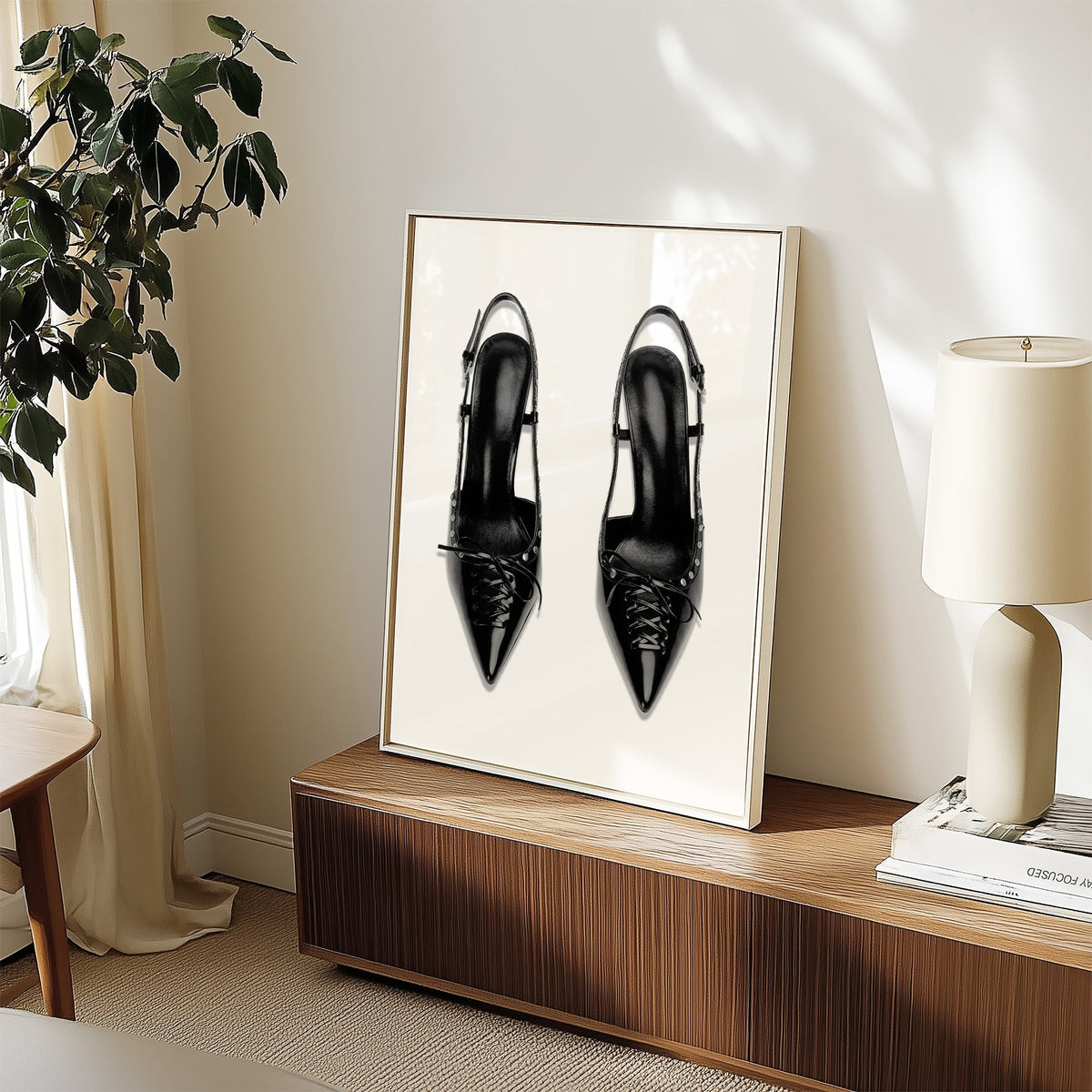 Black lace-up studded slingback heels print in a white frame on a walnut sideboard beside a ceramic lamp