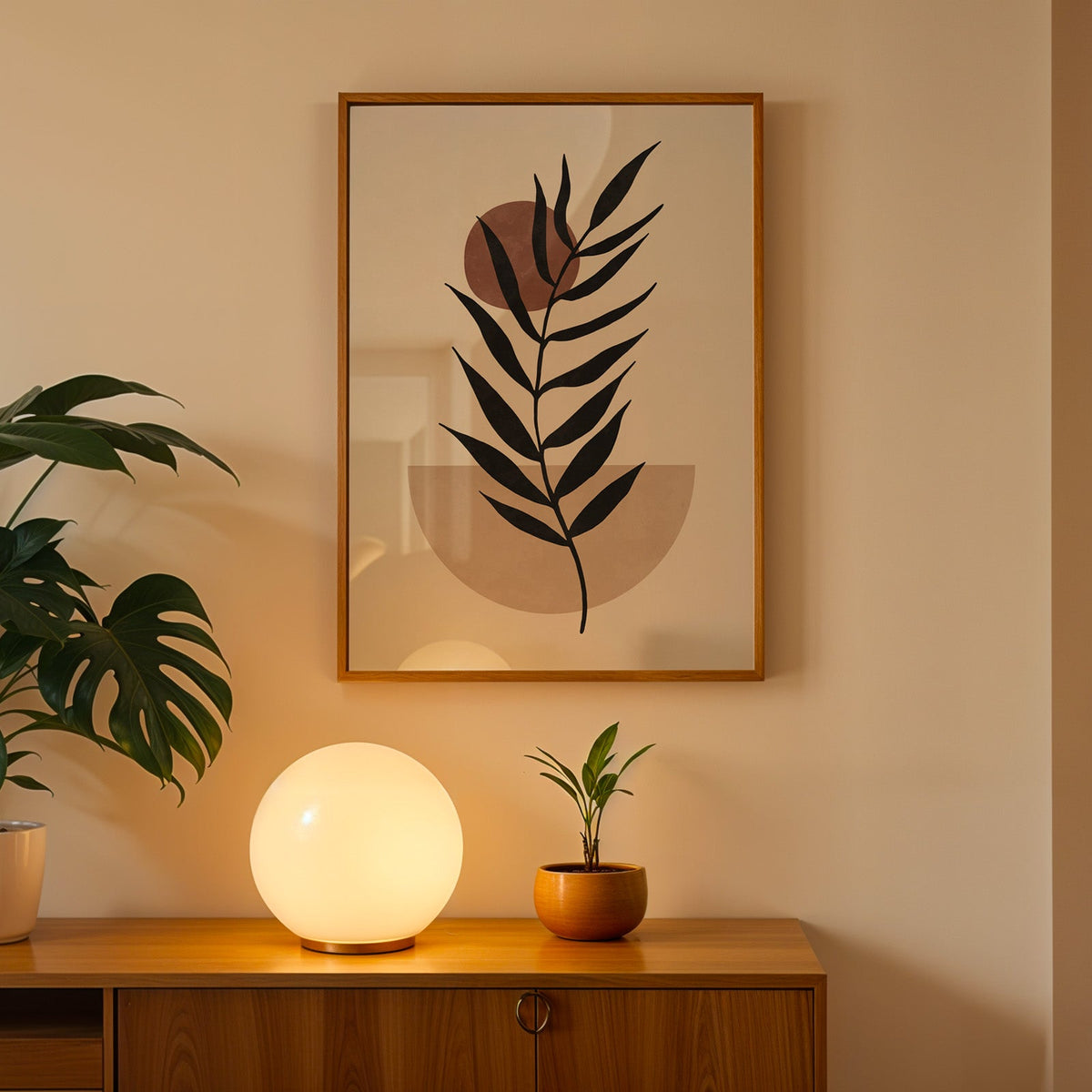Black leaf branch with rust sun boho print in an oak frame above a teak cabinet with a globe lamp and monstera