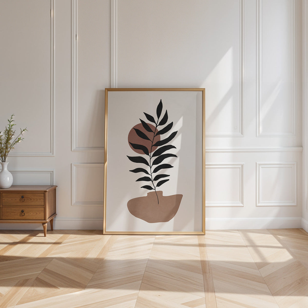 Black leaf branch and terracotta sun boho print shown in a gold frame leaning on a paneled white wall in sunlight
