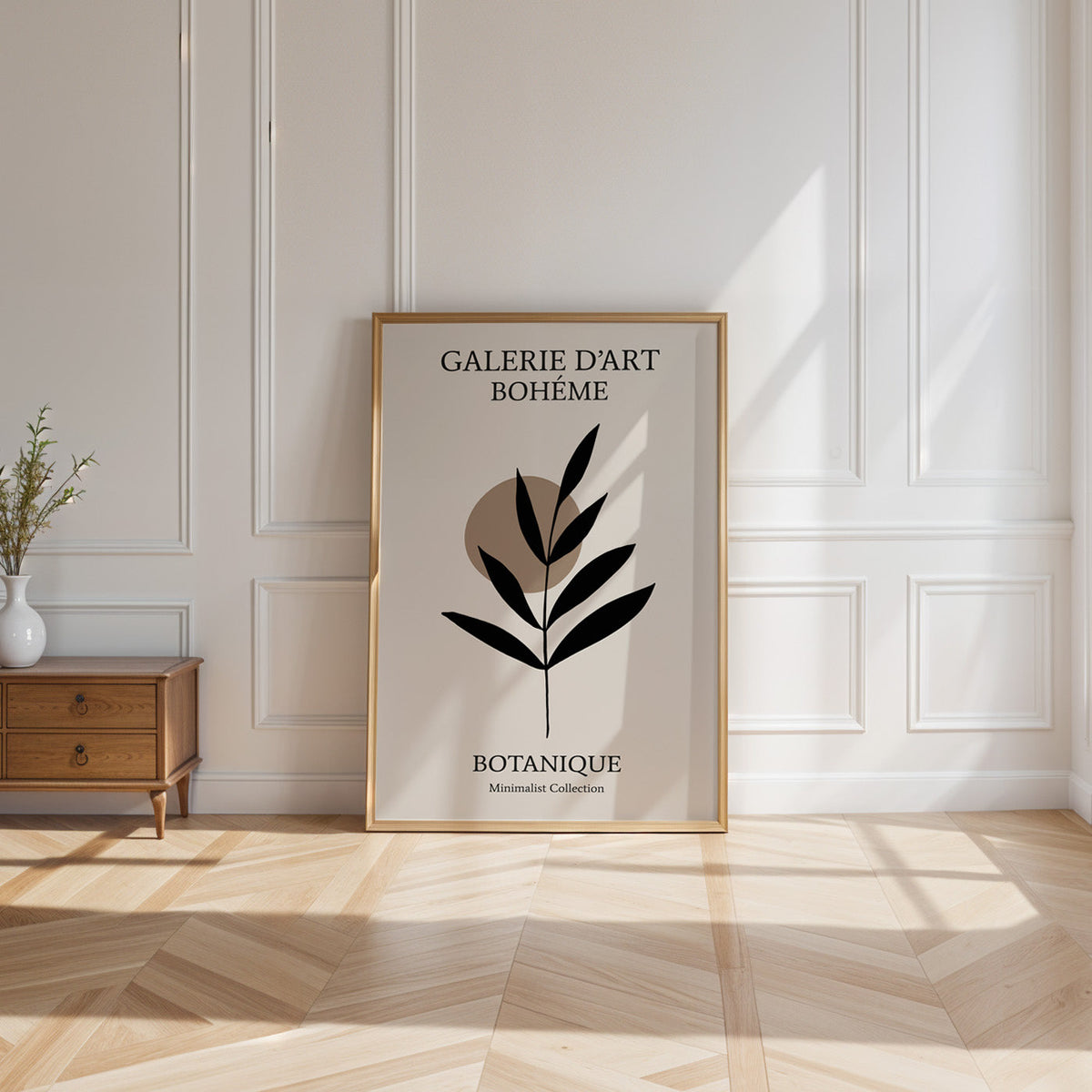 Black leaf sprig and taupe circle boho print shown in a gold frame leaning on a paneled white wall in sunlight