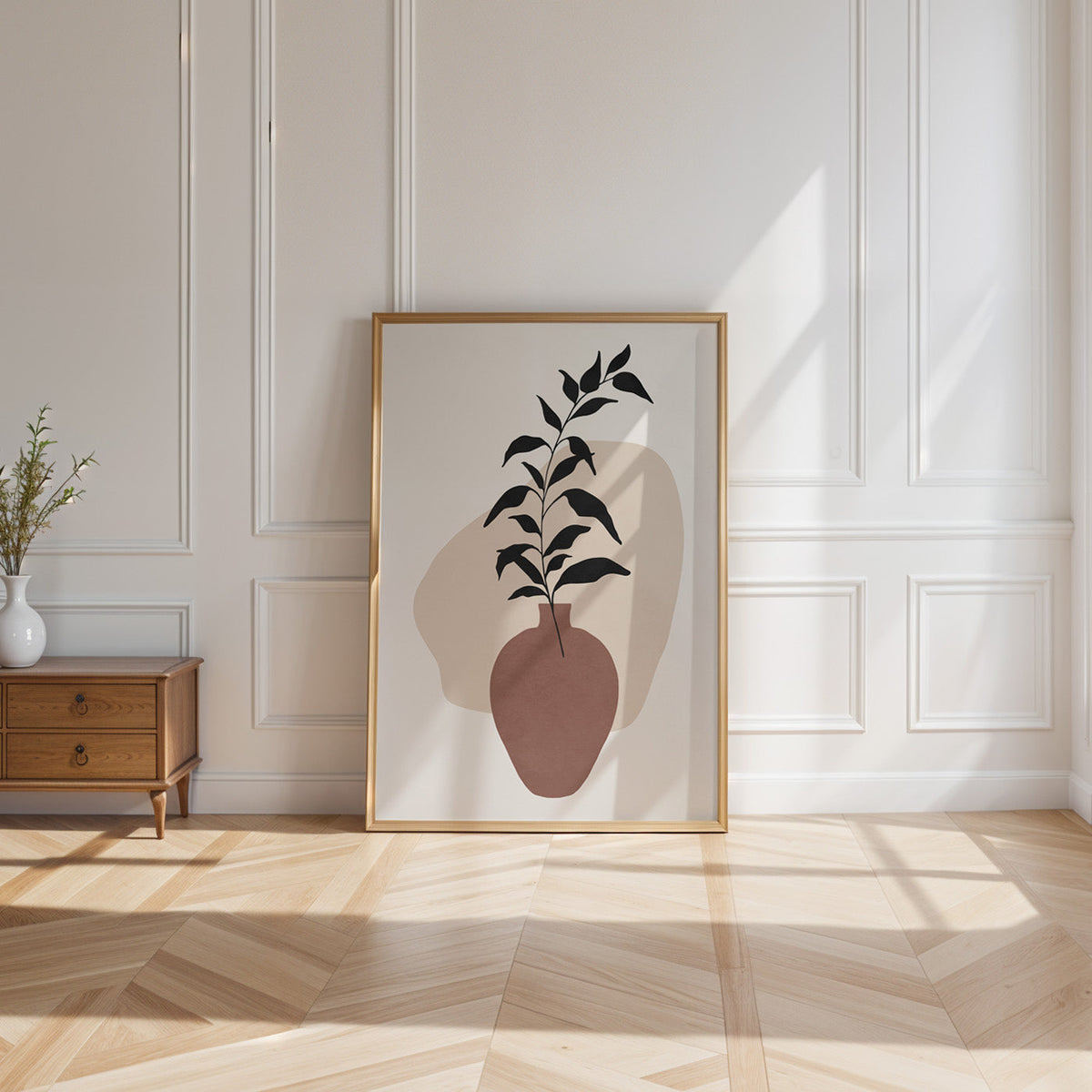 Black leaves in rosewood vase boho print shown in a gold frame leaning on a paneled white wall in sunlight