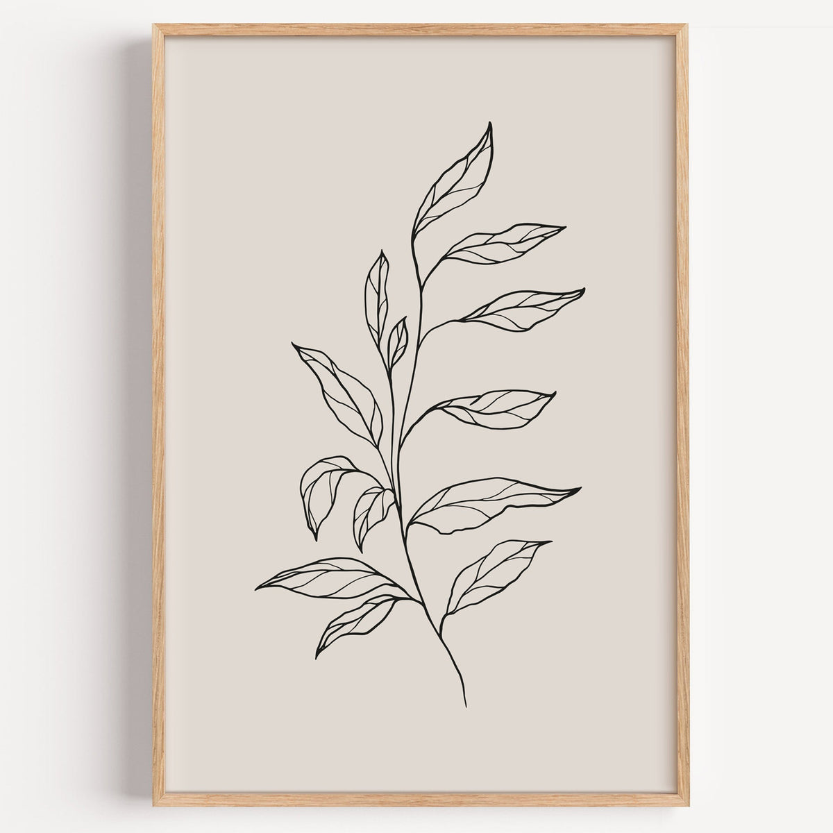 Black line leafy branch botanical line art print in a light oak frame on a plain white wall