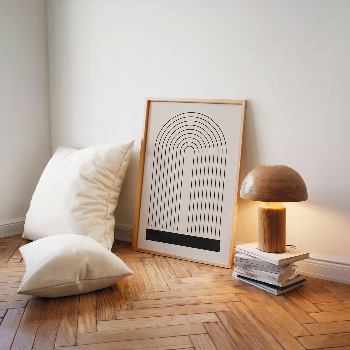 Black line rainbow arch minimalist print in a light wood frame on a herringbone floor by a wooden mushroom lamp