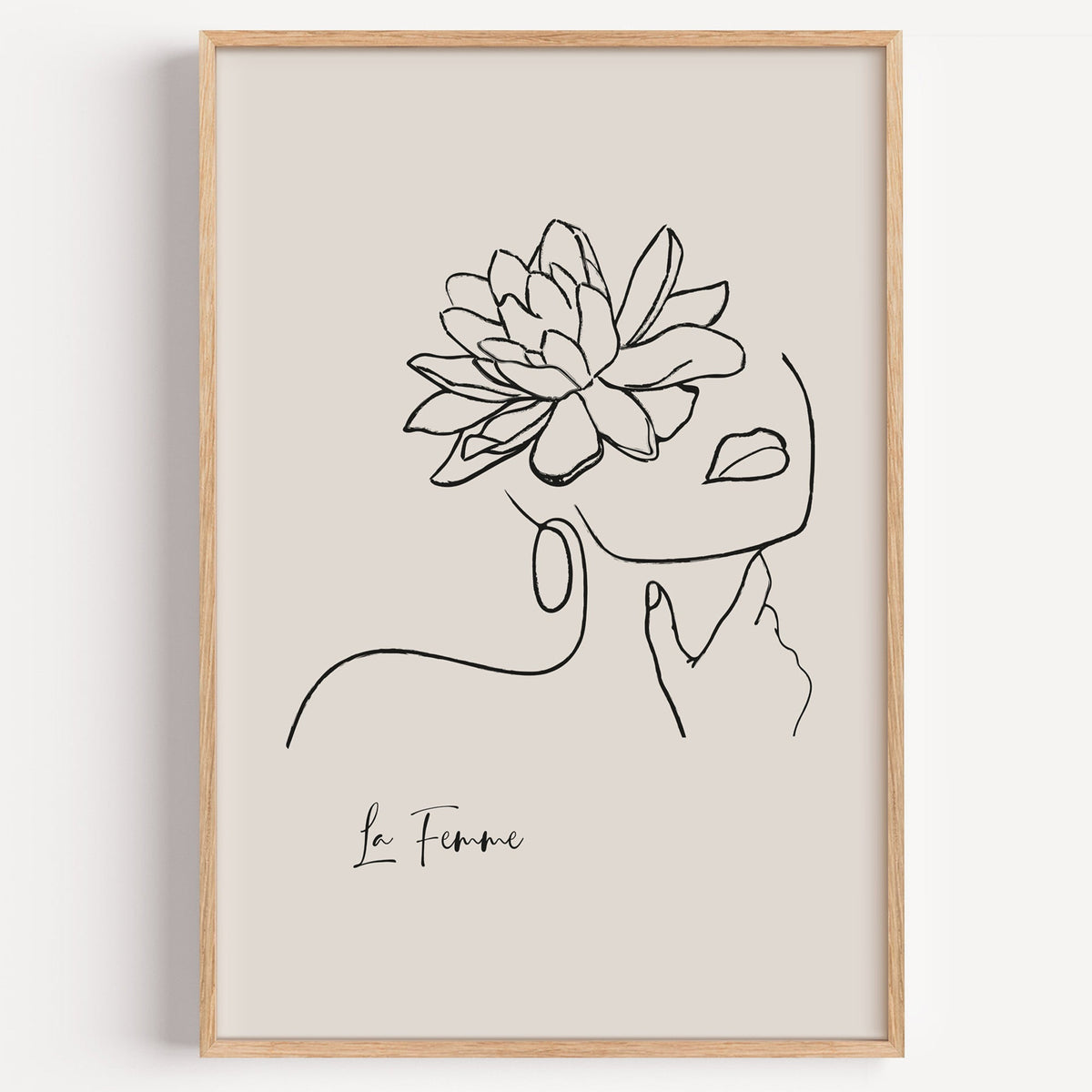 Woman face and flower black line art print in a light oak frame on a plain white wall