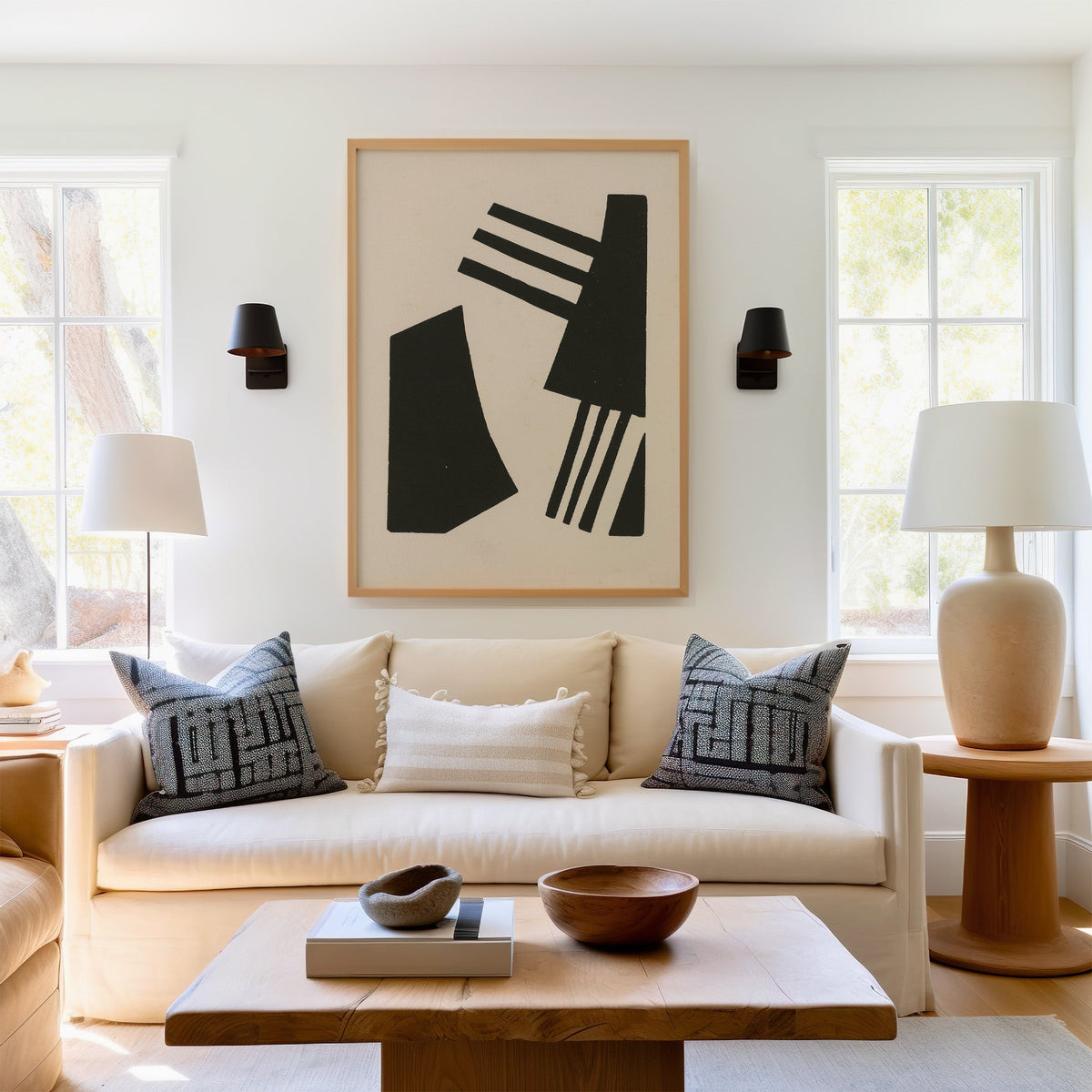 Black linocut comb shapes print in a light oak frame above a cream sofa between two black wall sconces