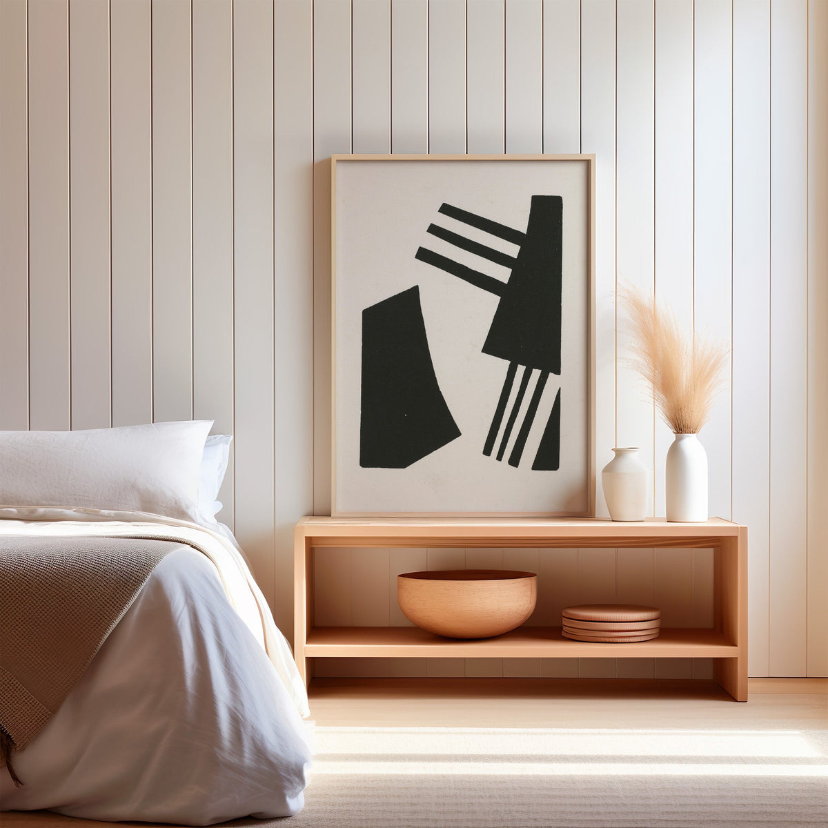 Black linocut comb shapes print in a light oak frame on a wood bench by a bed with pampas grass