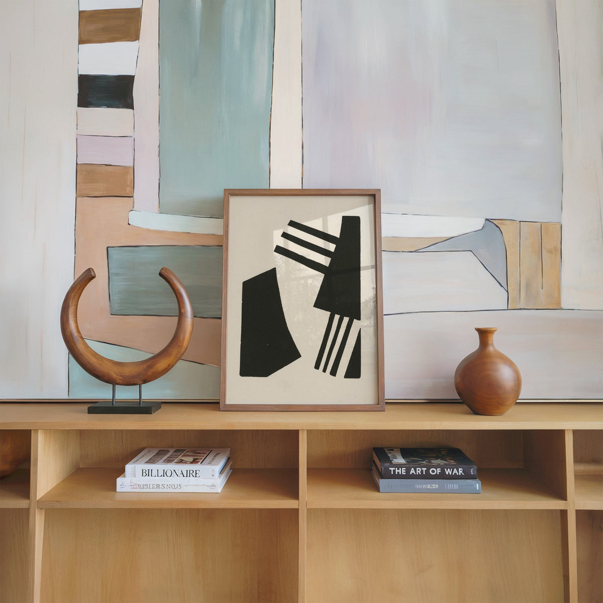 Black linocut comb shapes print in a walnut frame on an oak shelf beside a wooden crescent sculpture