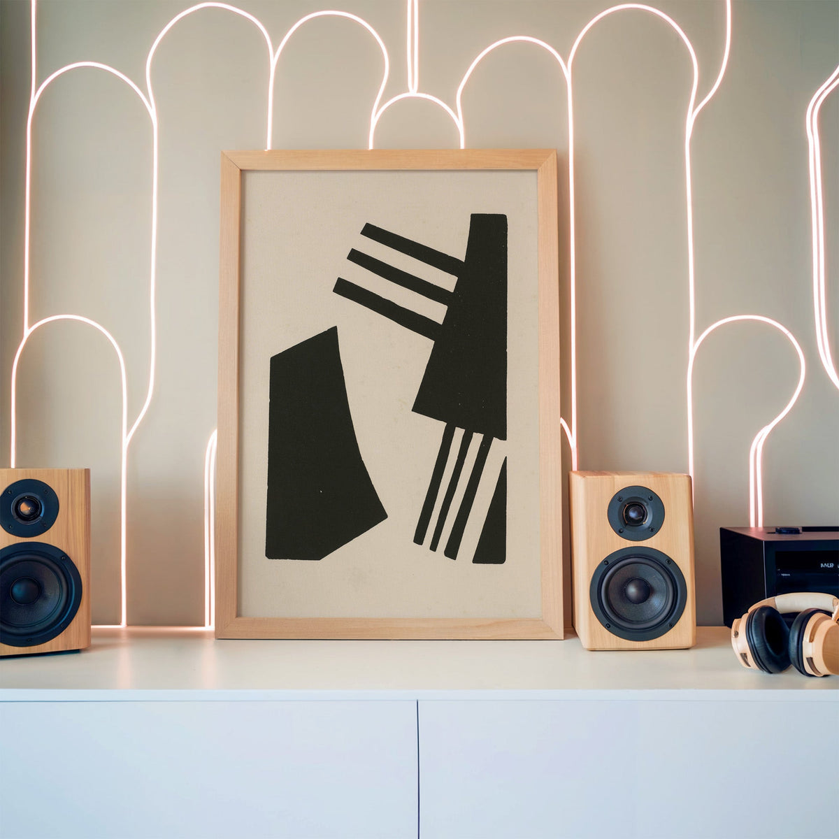 Black linocut comb shapes print in a pine frame between wooden speakers by a neon arch light wall