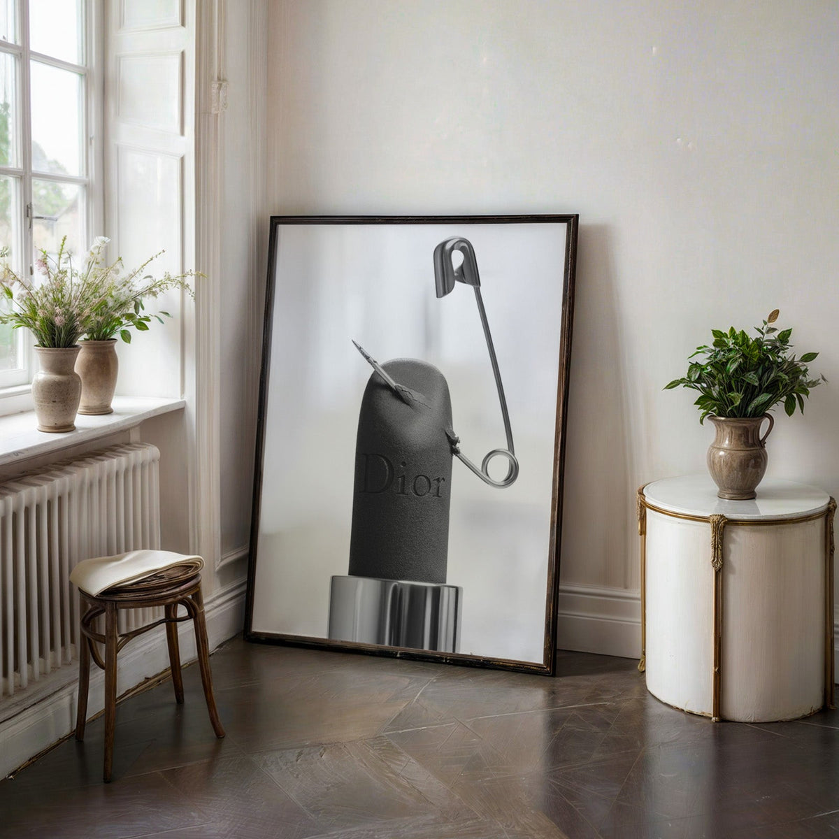 Matte black lipstick pierced by safety pin print in a black frame on a dark stone floor beside a white side table