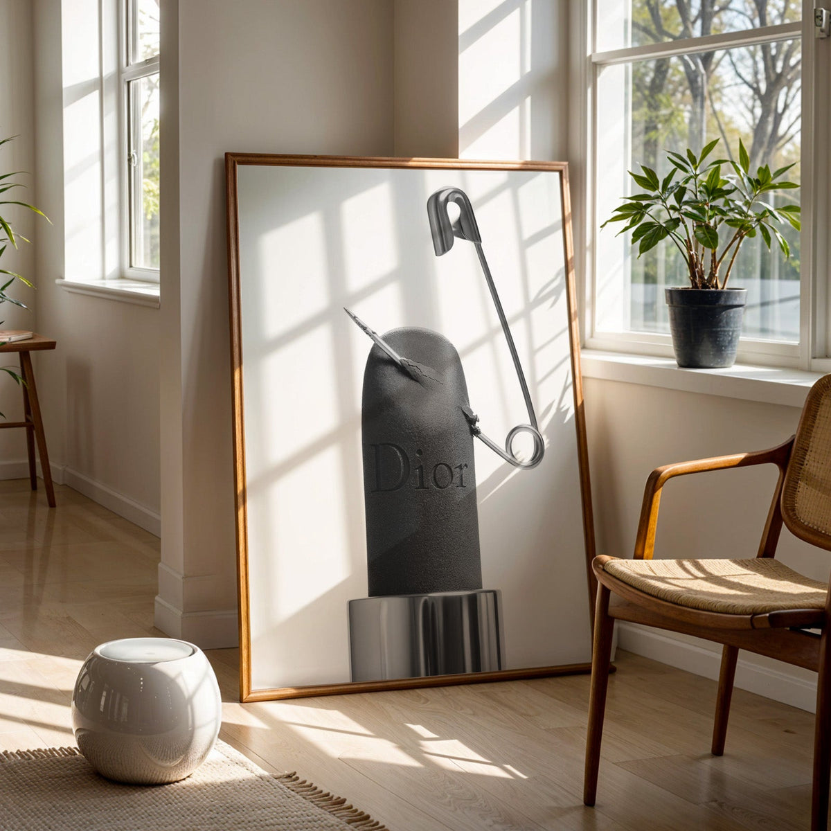 Matte black lipstick pierced by safety pin print in a walnut frame on a wood floor beside a cane chair and sunny window