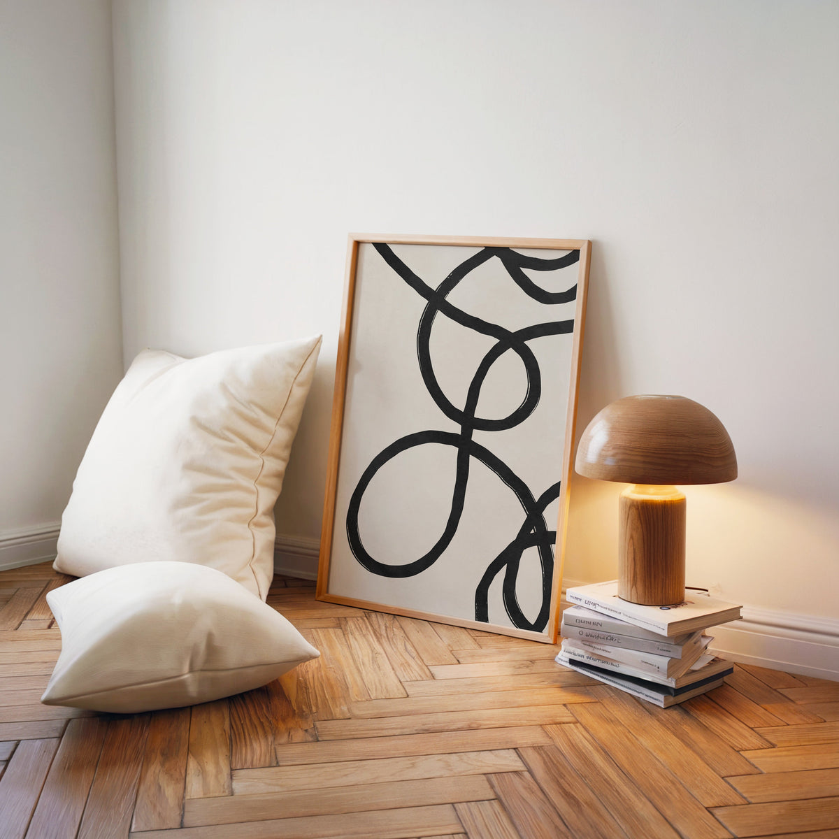 Black looping brushstroke lines minimalist print in a light wood frame on a herringbone floor by a wooden mushroom lamp