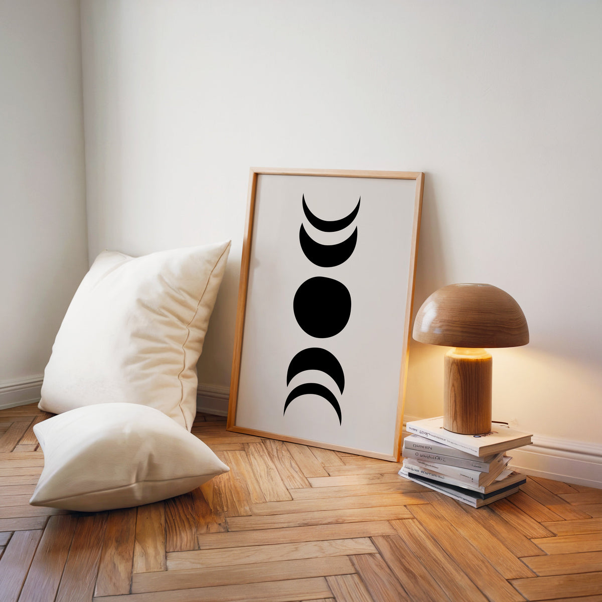 Black organic moon phases minimalist print in a light wood frame on a herringbone floor by a wooden mushroom lamp