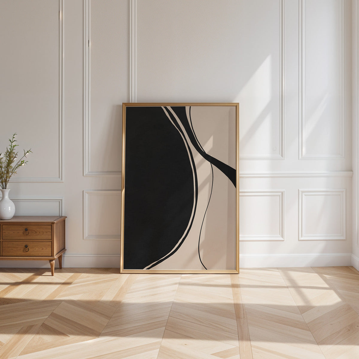 Black organic shape and flowing lines minimalist print shown in a gold frame leaning on a paneled white wall in sunlight