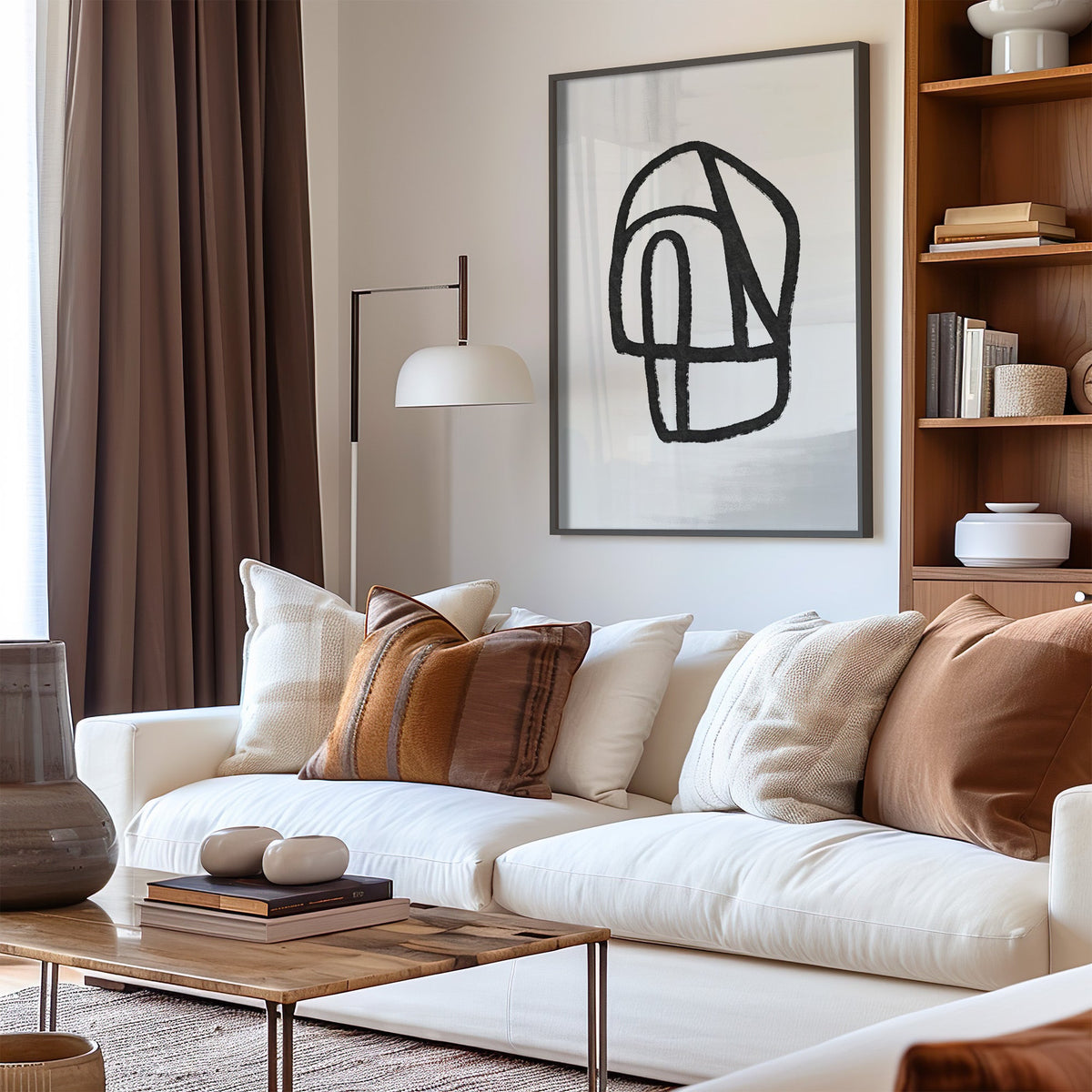 Black outline segmented pebble shape print in a black frame above a cream sofa with brown striped pillows