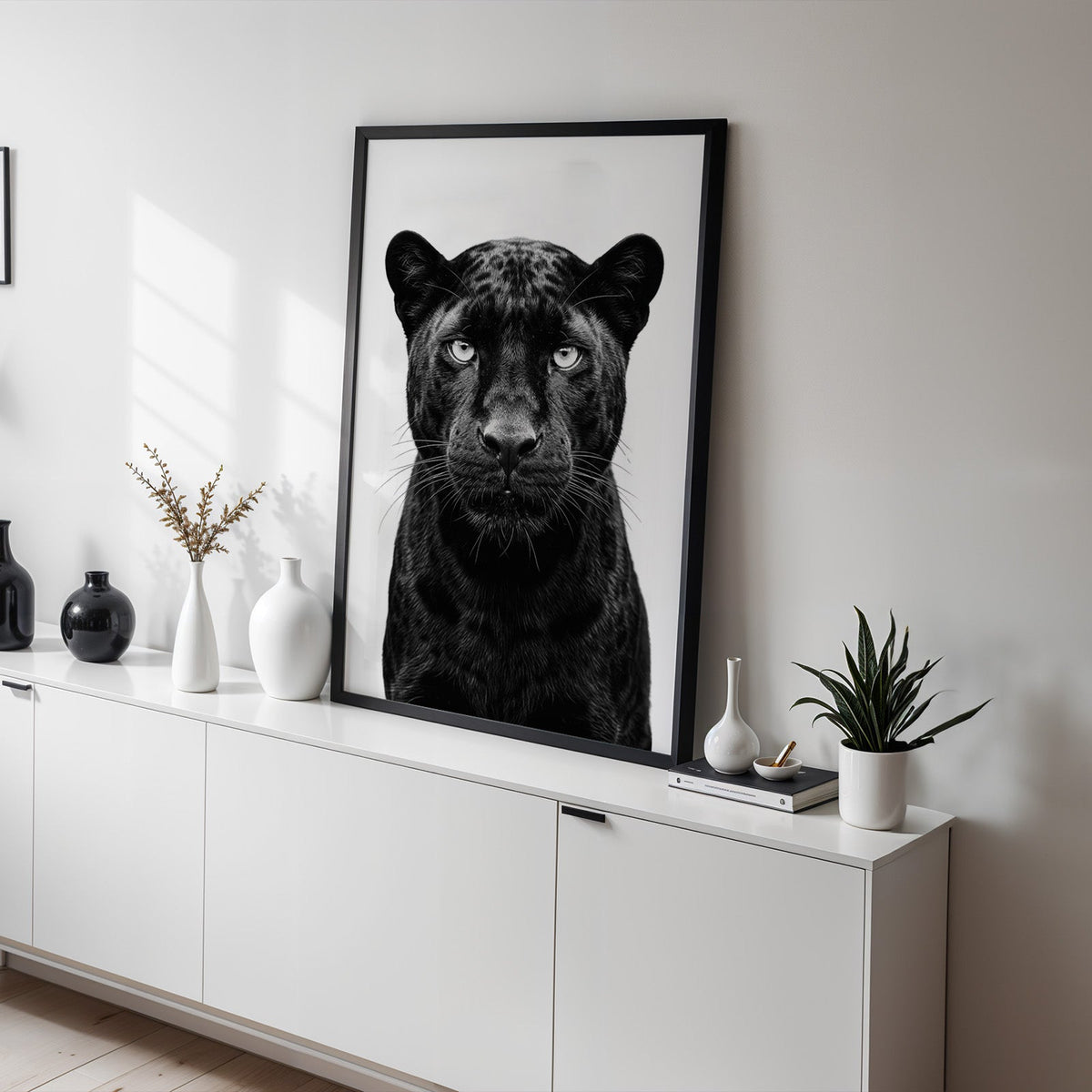 Front-facing black panther portrait on white print in a black frame on a white sideboard with black and white vases