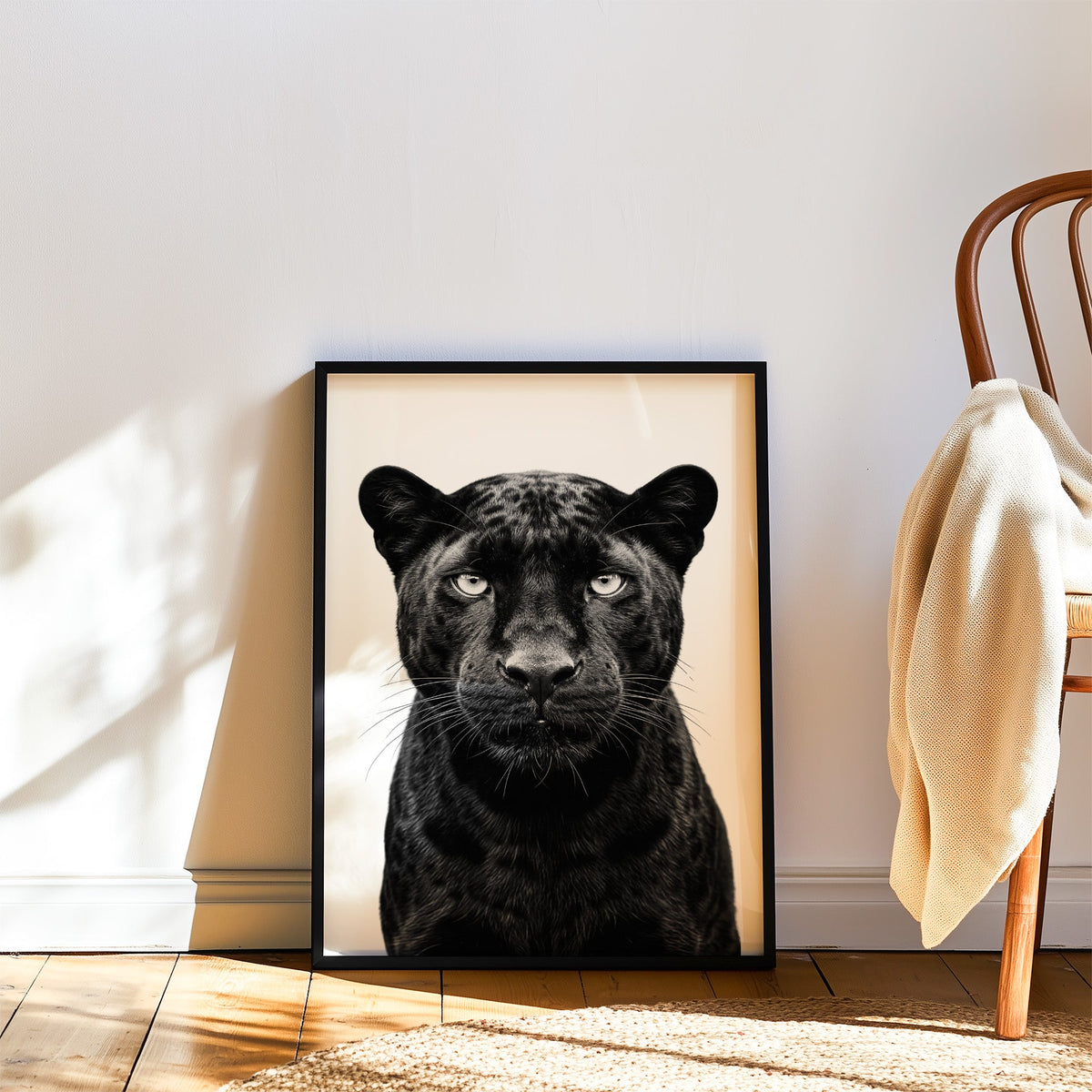 Front-facing black panther portrait on white print in a black frame leaning on a wood floor beside a bentwood chair