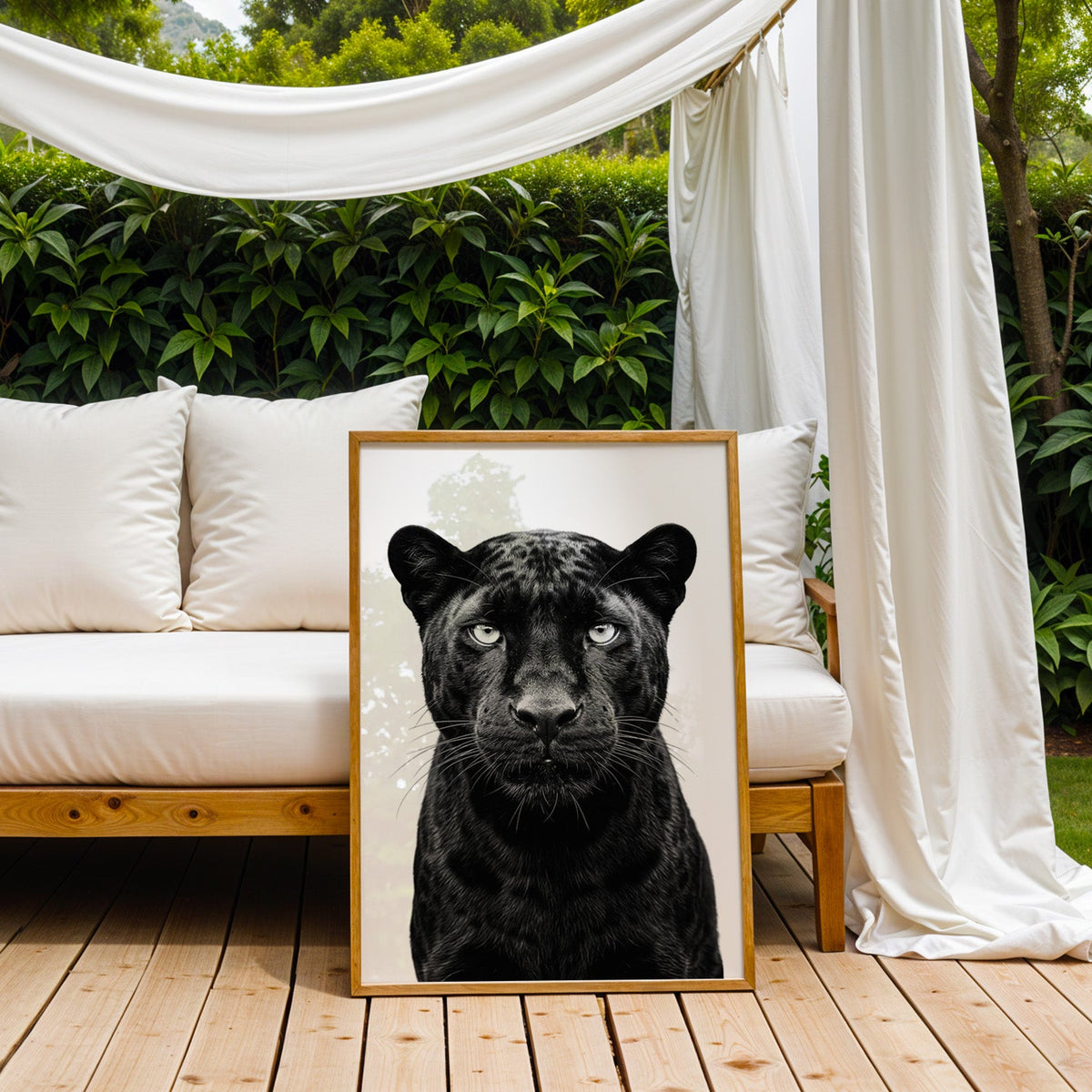 Front-facing black panther portrait on white print in an oak frame on an outdoor daybed under white drapes