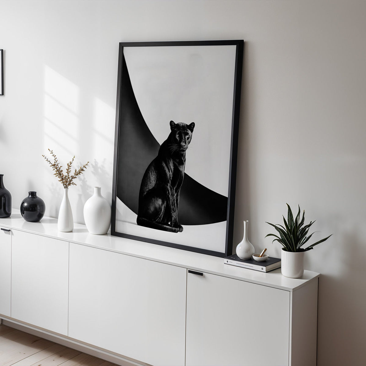 Seated black panther in front of black arc print in a black frame on a white sideboard with black and white vases